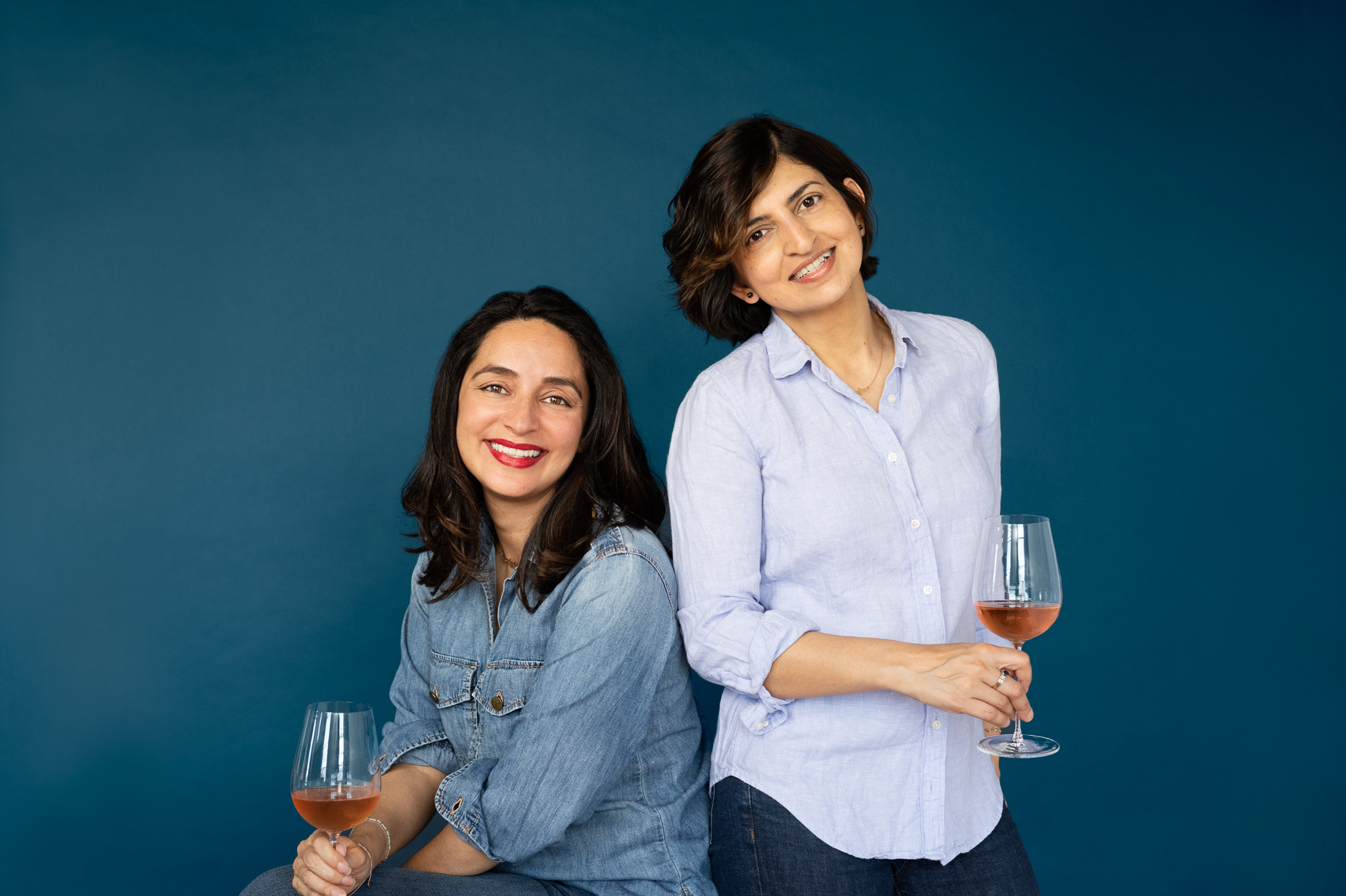 Rubyna and Gabriela, Founders of Levavoce Vino, holding glasses of wine on a blue background. | Wohler & Co. Maine Portrait Studio