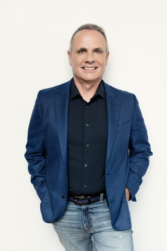 Mike Thorne, Leadership Coach, standing in black button down shirt and blue blazer, against white wall.