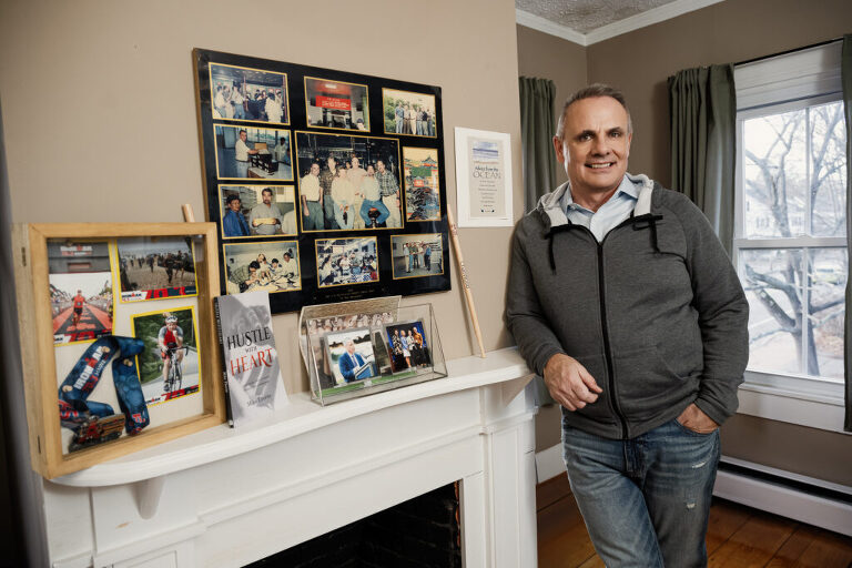 Mike Thorne, leadership coach, leaning on a fireplace with personal photos and memorabilia on the shelf.