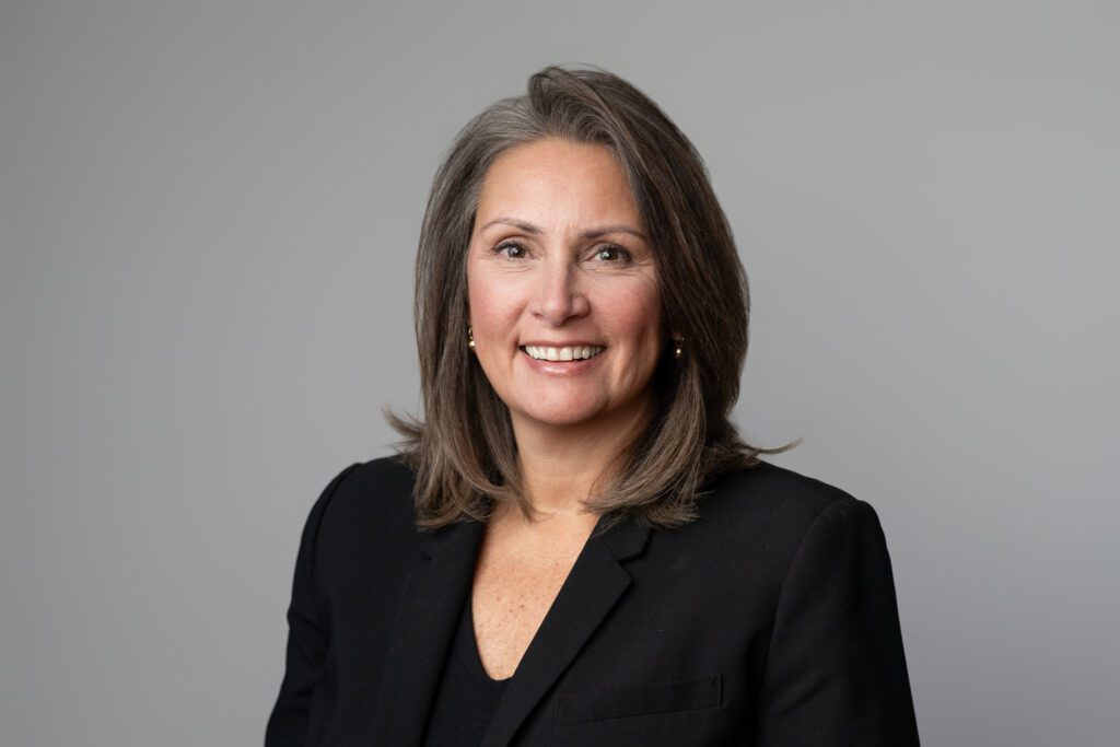 Headshot of a woman wearing a black blazer and shirt for United Insurance, standing in front of light gray background. Taken by Wohler & Co.