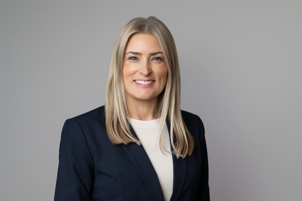 Headshot of a woman with blonde hair wearing a cream shirt with navy blazer for United Insurance, standing in front of light gray background. Taken by Wohler & Co.